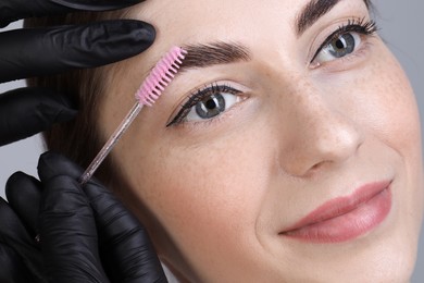 Photo of Brow lamination. Cosmetologist combing woman's eyebrows with brush, closeup