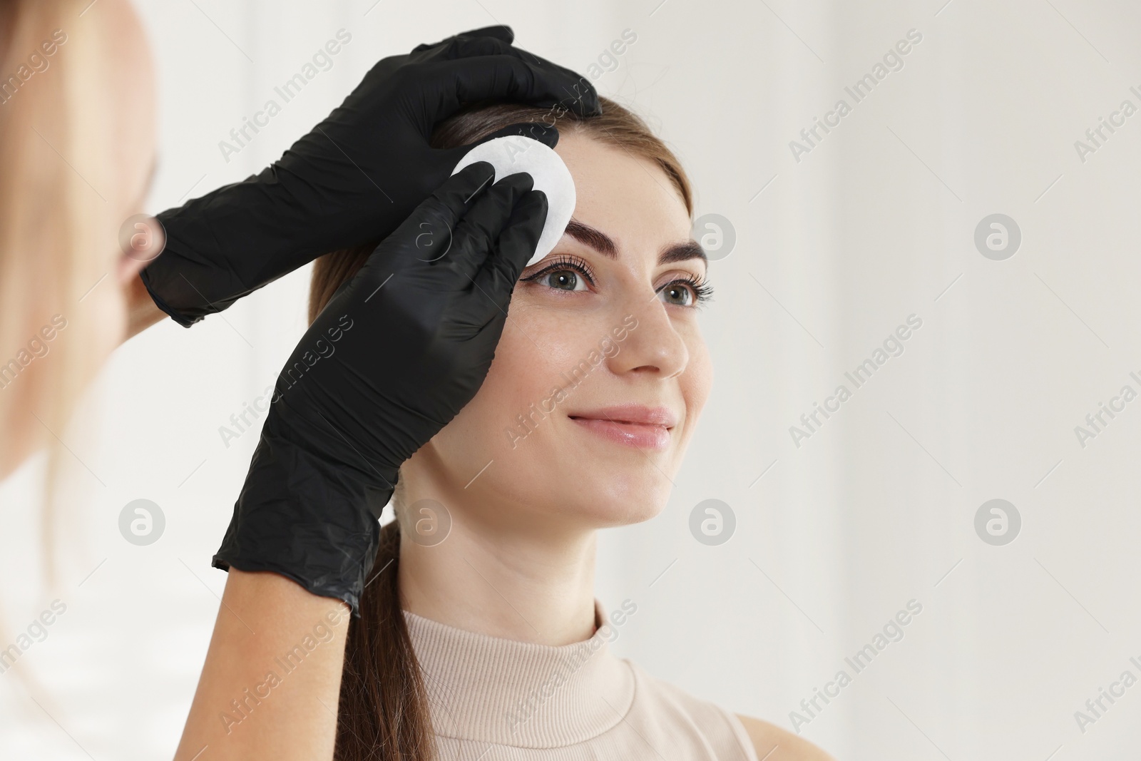 Photo of Beautician wiping client`s eyebrows after henna dyeing in salon