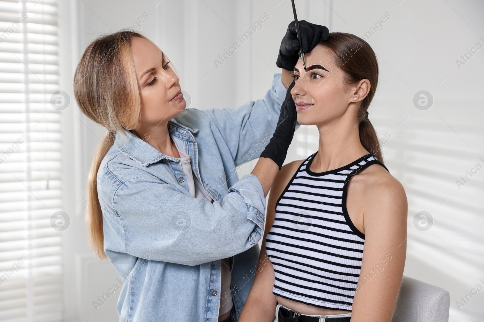 Photo of Beautician dyeing client’s eyebrows with henna in salon