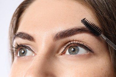 Beautiful young woman after henna eyebrows dyeing on light background, closeup