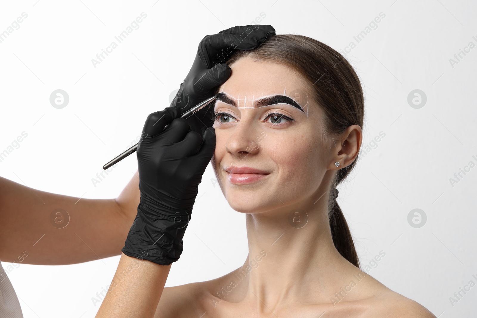 Photo of Young woman undergoing henna eyebrows dyeing procedure on white background, closeup