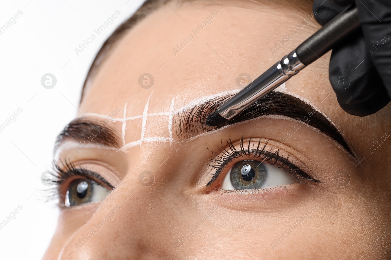 Photo of Young woman undergoing henna eyebrows dyeing on light background, closeup