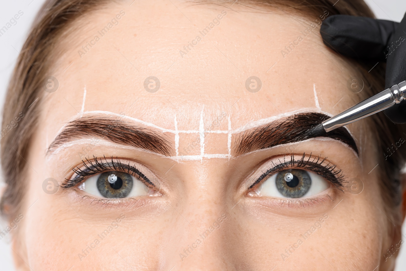 Photo of Young woman undergoing henna eyebrows dyeing procedure, closeup