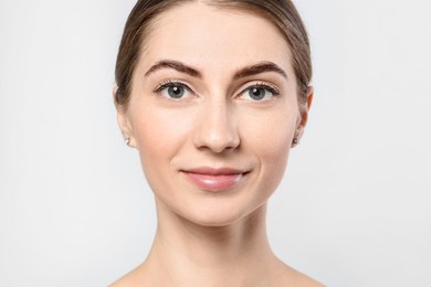 Beautiful young woman after henna eyebrows dyeing on light background, closeup