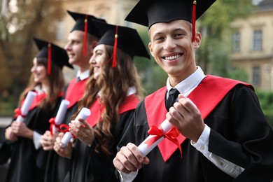 Photo of Happy students with diplomas after graduation ceremony outdoors, selective focus