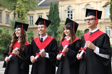 Photo of Happy students with diplomas after graduation ceremony outdoors