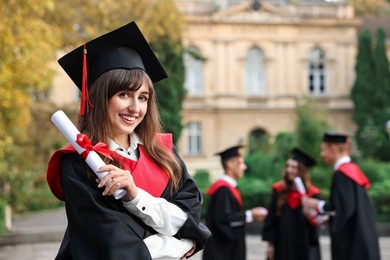 Photo of Happy students with diplomas after graduation ceremony outdoors, selective focus