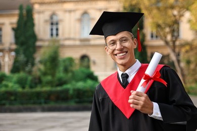 Happy student with diploma after graduation ceremony outdoors, space for text