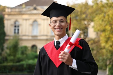 Photo of Happy student with diploma after graduation ceremony outdoors