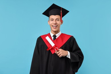 Happy student with diploma after graduation on light blue background