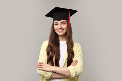 Happy student with crossed arms after graduation on grey background