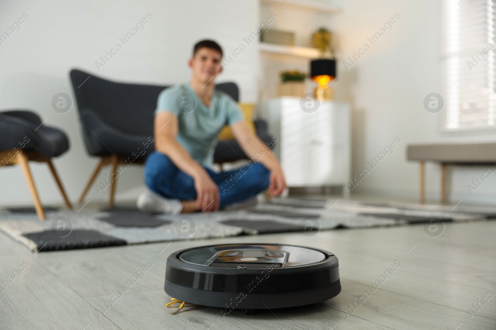 Photo of Robotic vacuum cleaner cleaning floor while man relaxing at home, selective focus