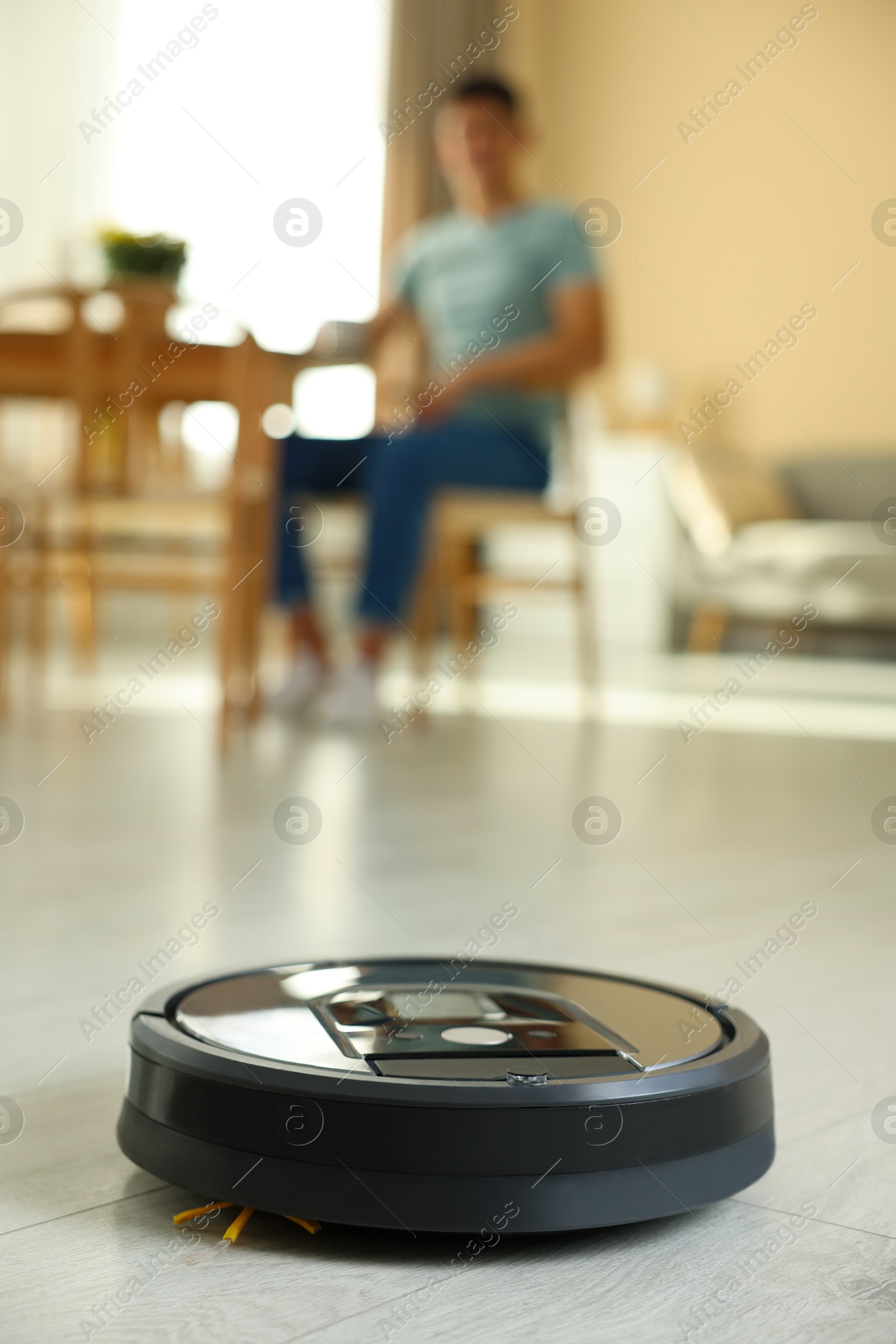 Photo of Robotic vacuum cleaner cleaning floor while man relaxing at home, selective focus