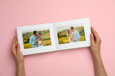 Woman looking at photos in photo album on pink background, top view