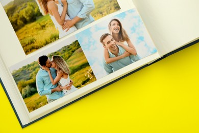 Photo of Open photo album with different photos on yellow background, top view