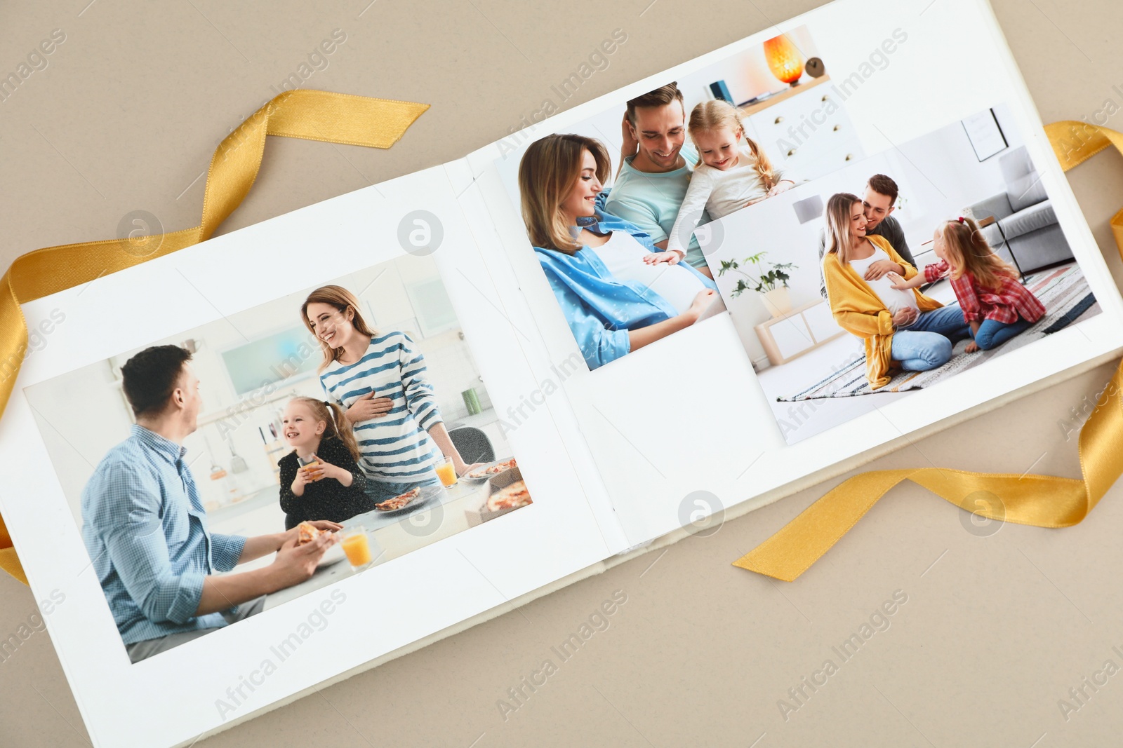 Photo of Open photo album with different photos and ribbon on beige background, top view