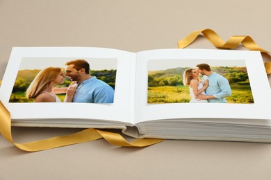 Open photo album with photos and ribbon on beige background