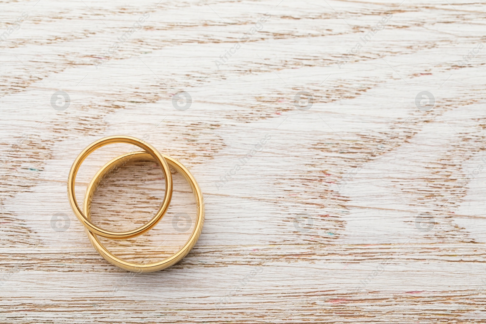 Photo of Beautiful golden wedding rings on wooden table, top view. Space for text