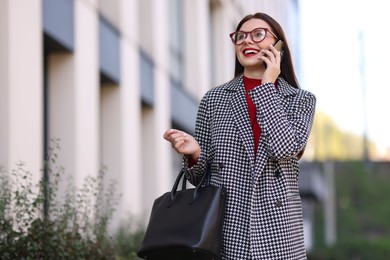 Photo of Beautiful woman in stylish suit talking on smartphone outdoors. Space for text