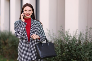 Beautiful woman in stylish suit talking on smartphone outdoors. Space for text