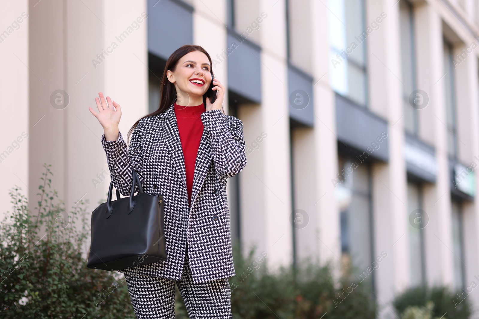 Photo of Smiling businesswoman in stylish suit talking on smartphone outdoors, low angle view. Space for text