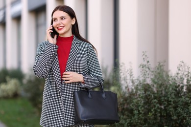 Beautiful woman in stylish suit talking on smartphone outdoors. Space for text