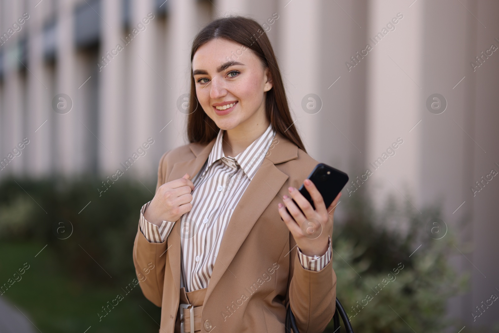 Photo of Smiling businesswoman in stylish suit with smartphone outdoors