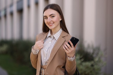 Photo of Smiling businesswoman in stylish suit with smartphone outdoors