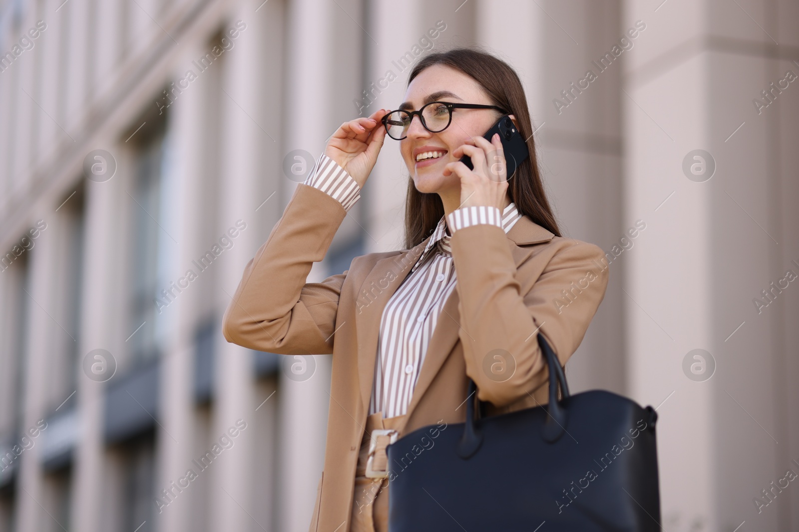 Photo of Smiling businesswoman in stylish suit talking on smartphone outdoors