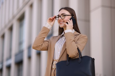 Photo of Smiling businesswoman in stylish suit talking on smartphone outdoors