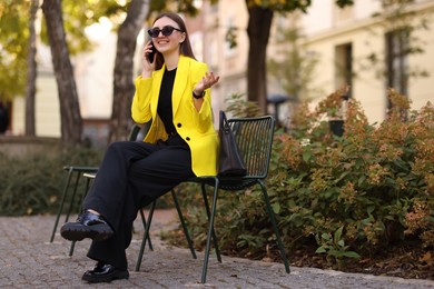 Smiling businesswoman in stylish suit talking on smartphone outdoors, low angle view. Space for text