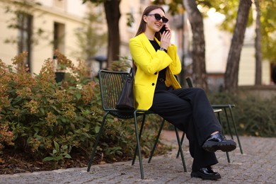 Photo of Smiling businesswoman in stylish suit talking on smartphone outdoors, low angle view. Space for text