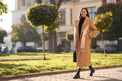 Smiling businesswoman in stylish suit walking outdoors. Space for text