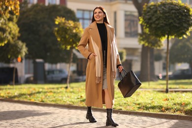 Smiling businesswoman in stylish suit walking outdoors. Space for text