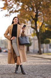 Photo of Smiling businesswoman in stylish suit with smartphone outdoors, low angle view