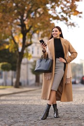 Smiling businesswoman in stylish suit with smartphone outdoors, low angle view