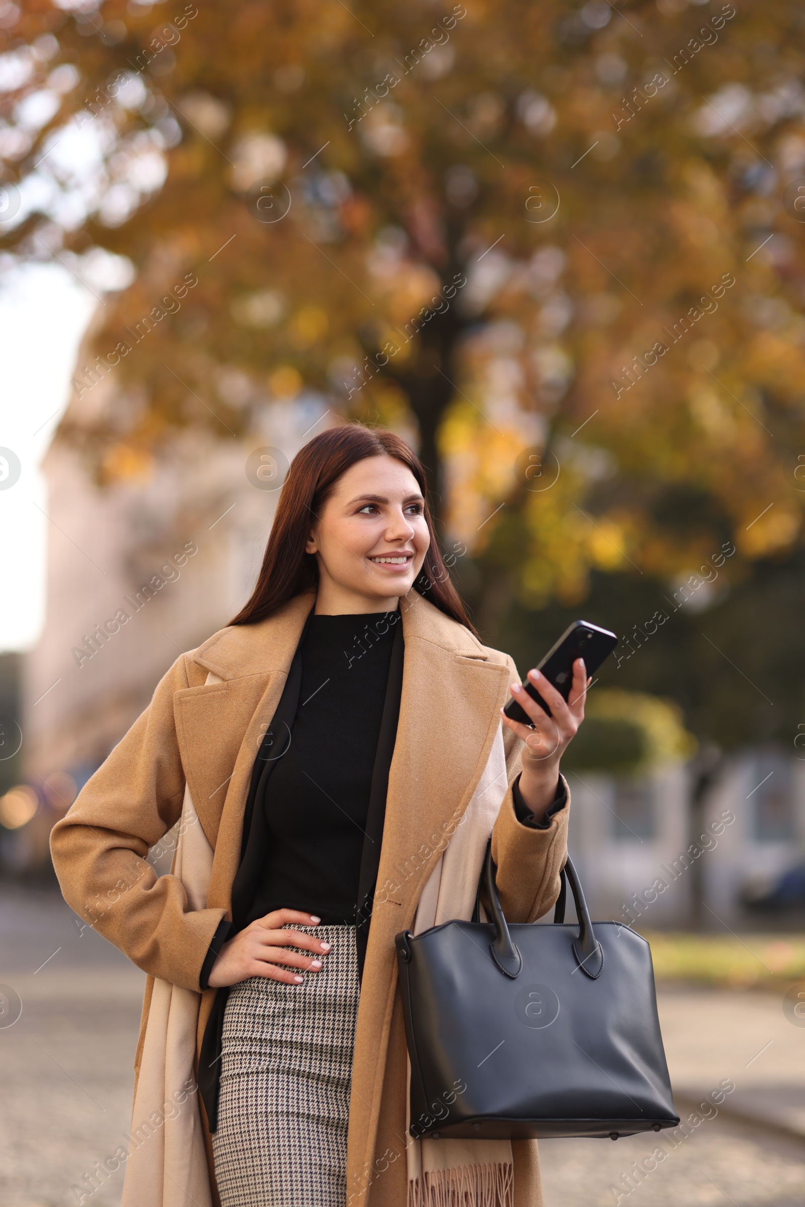 Photo of Smiling businesswoman in stylish suit with smartphone outdoors