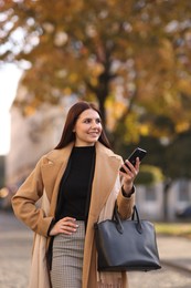 Smiling businesswoman in stylish suit with smartphone outdoors