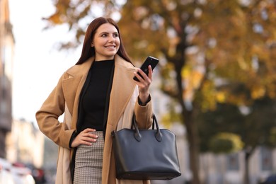 Photo of Smiling businesswoman in stylish suit with smartphone outdoors, low angle view. Space for text