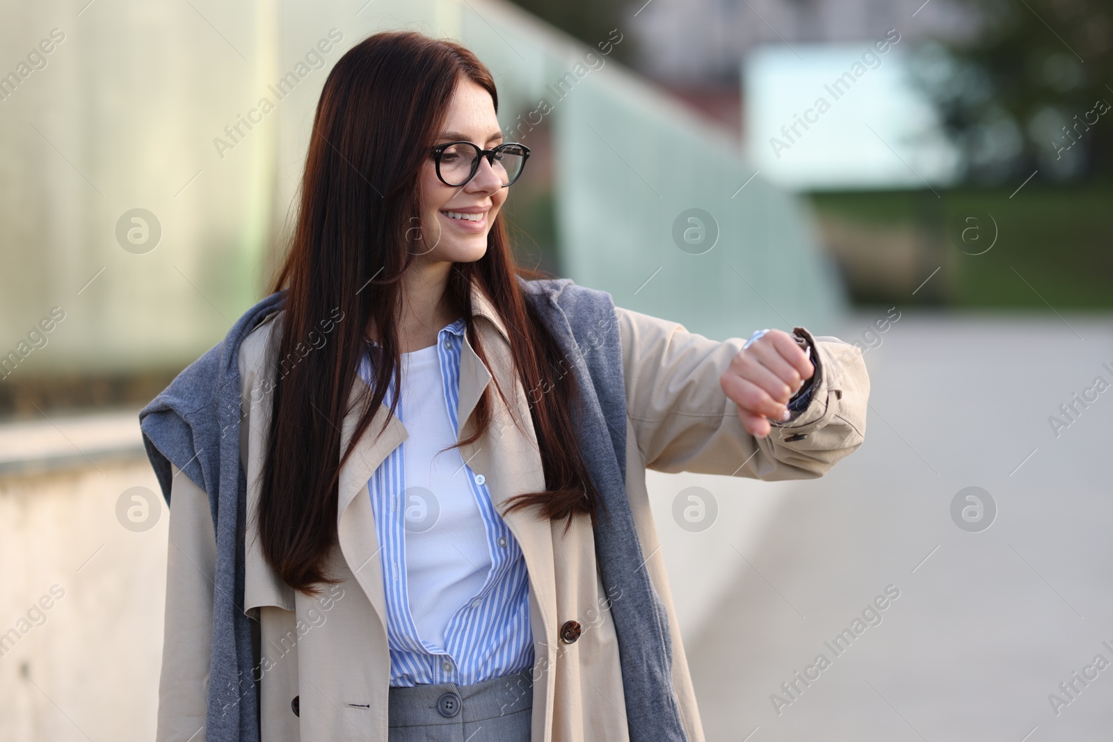 Photo of Smiling businesswoman in stylish suit looking at wristwatch outdoors