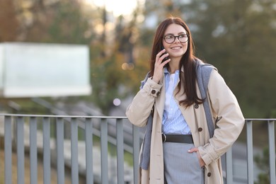 Beautiful woman in stylish suit talking on smartphone outdoors. Space for text