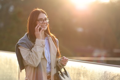 Photo of Smiling businesswoman in stylish suit talking on smartphone outdoors at morning. Space for text