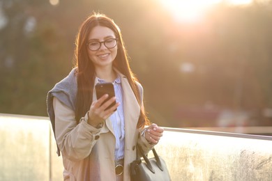 Smiling businesswoman in stylish suit with smartphone outdoors at morning. Space for text