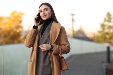 Photo of Businesswoman in stylish suit talking on smartphone outdoors. Space for text