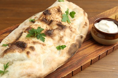 Photo of Board with tasty calzone, parsley and sauce on wooden table, closeup