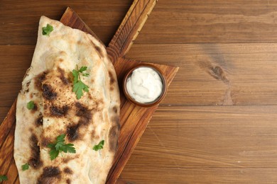 Photo of Board with tasty calzone, parsley and sauce on wooden table, top view. Space for text