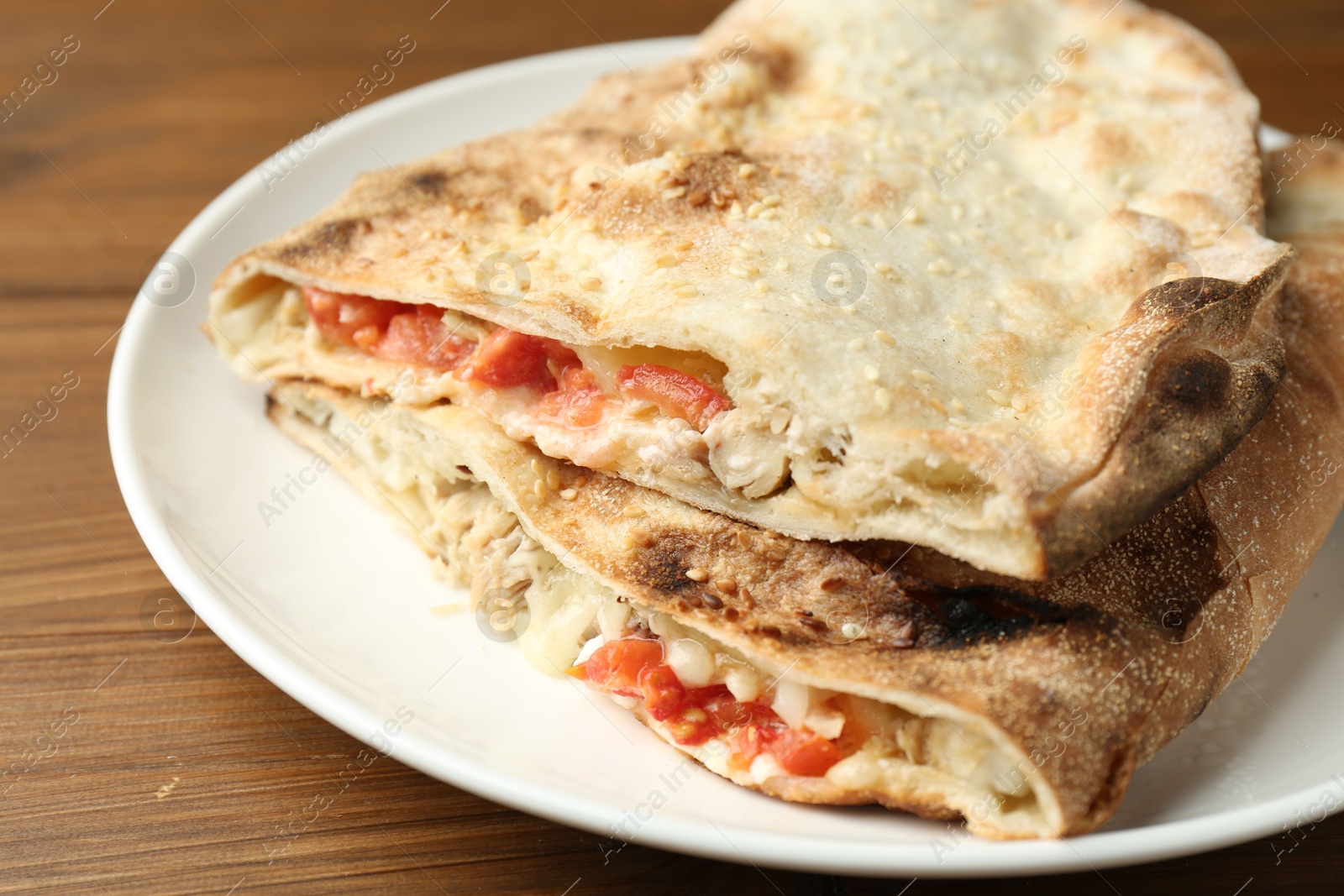 Photo of Halves of tasty calzone with meat, cheese and tomato on wooden table, closeup