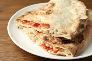 Halves of tasty calzone with meat, cheese and tomato on wooden table, closeup