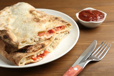 Photo of Halves of tasty calzone with meat, cheese and tomato served with sauce on wooden table, closeup