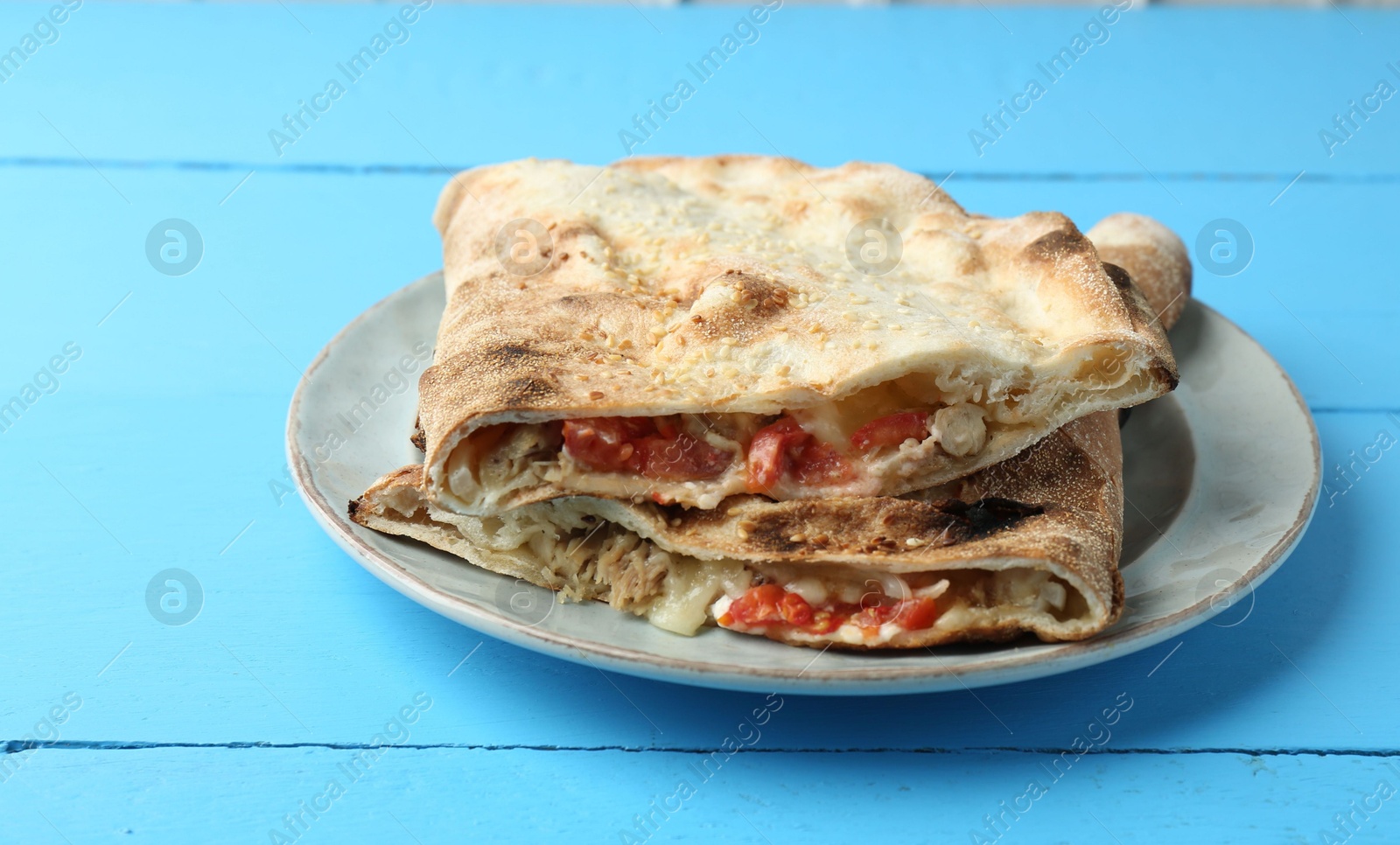 Photo of Halves of tasty calzone with meat, cheese and tomato on light blue wooden table, closeup